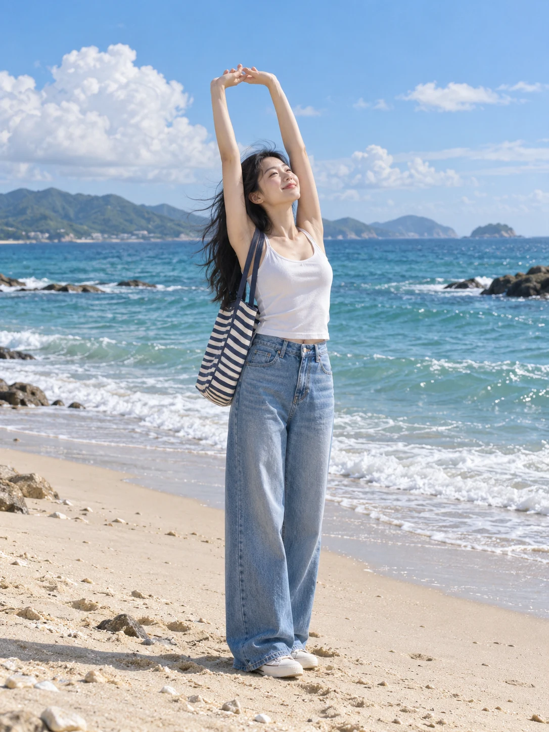 Adult East Asian woman in a white tank top and blue jeans stretching both hands overhead on a beach